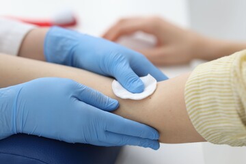 Fototapeta premium Nurse disinfecting patient's arm before drawing blood sample at white table in clinic, closeup