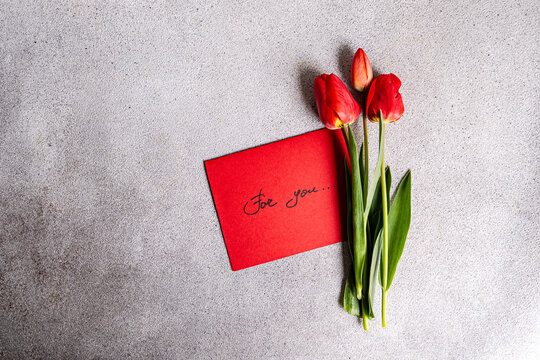 Red tulips with heartfelt card on concrete surface