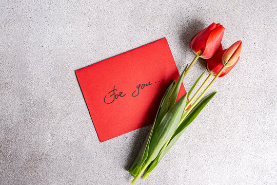 Red tulips with greeting card on textured surface