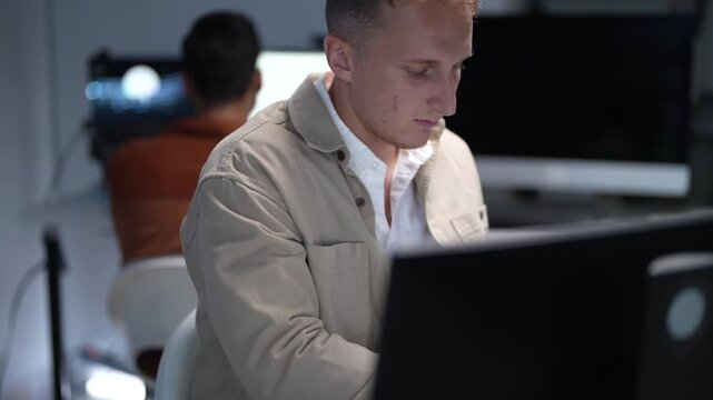 Focused young Caucasian businessman working on a computer screen during a late night software programming and creative startup development session in the office.