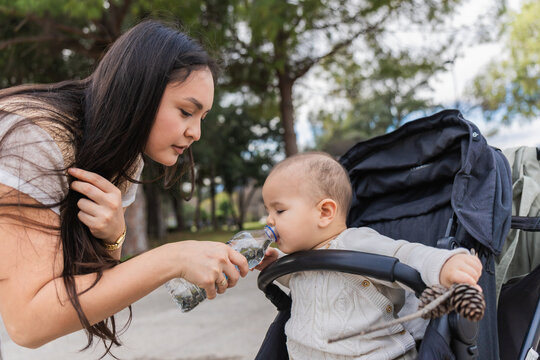 Mother offering water to child in stroller at park