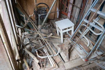 A cluttered shed filled with old metal objects, wood, and a small white stool. © DBA