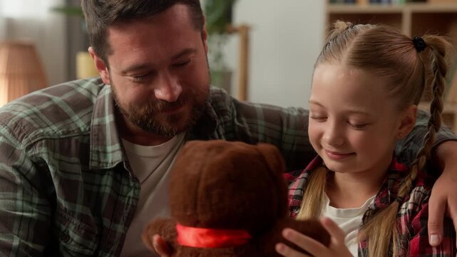 Happy Caucasian family child little girl hug toy teddy bear dad smiling at home cheerful schoolgirl daddy parent cuddling daughter birthday gift man guy kid celebrate father enjoying holiday bonding