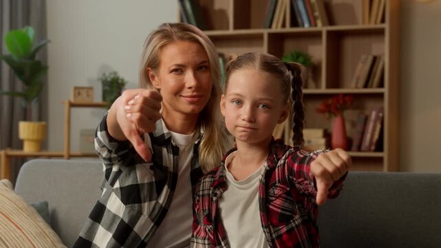 Caucasian family daughter woman mom showing thumb down refusal negative gesture child schoolgirl looking at camera upset little girl kid mother sad female parent denial no sign at home reject dislike