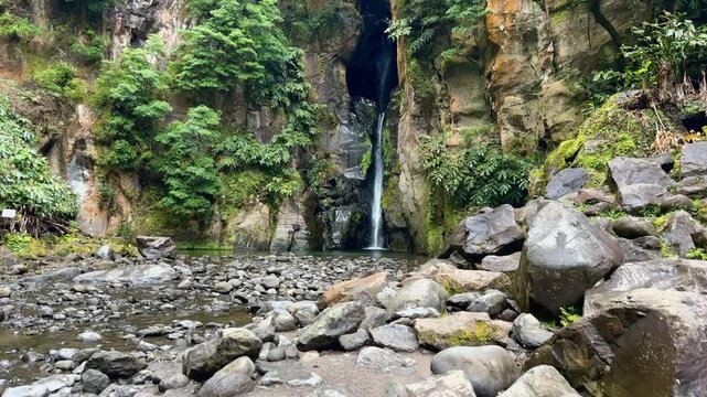 Footage of Salto do Cabrito Waterfall on S&atilde;o Miguel Island in the Azores, Portugal. Water cascades down volcanic rocks into a clear pool, surrounded by lush greenery and tropical forest, ideal for nat