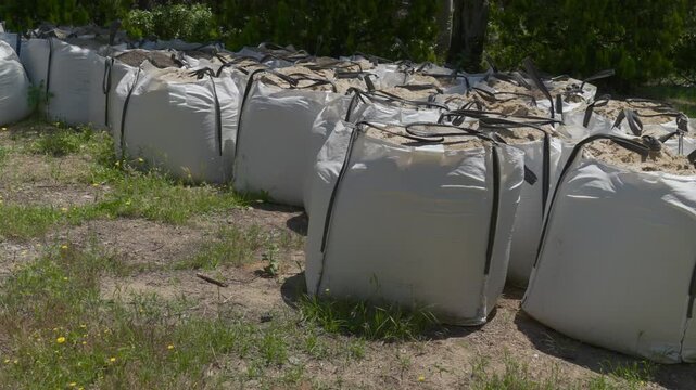 Large white bulk bags filled with soil and compost arranged in rows on grass for garden landscaping