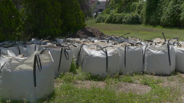 Large white builder's bags filled with topsoil and compost sitting on grass for landscaping work