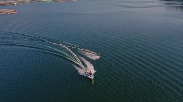 Cinematic drone shot of a speedboat towing a water skier across calm blue waters. Wide aerial perspective with ocean ripples, summer adventure, marine tourism and outdoor recreation.