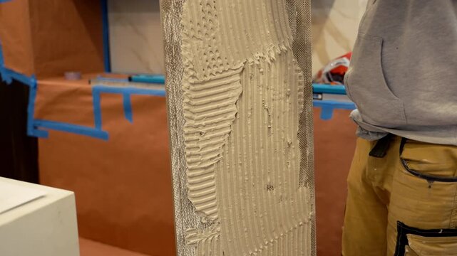 Professional worker applies thick layer of adhesive to ceramic tile to glue it to wall