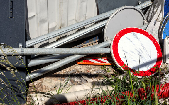 Dismounted traffic signs and metal poles piled up at a construction zone. Concept of road repairs, city infrastructure maintenance, and industrial storage.