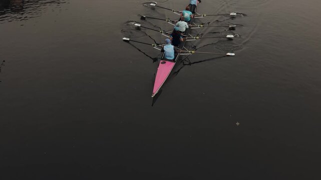 A long rowing boat glides across calm water, powered by synchronized rowers. Captured from above, this peaceful scene showcases teamwork, endurance, outdoor sport, and the beauty of recreational rowin