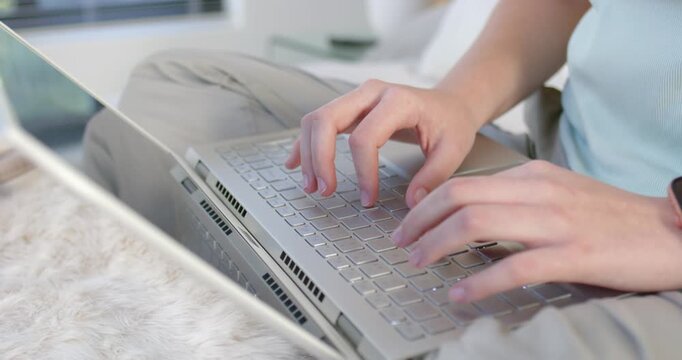 Adult female placing hands on keyboard, typing on silver laptop in bed to finish assignment