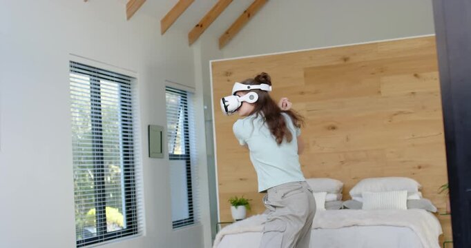 Woman wearing white VR headset adjusting head, swinging arms, following VR prompts in bedroom