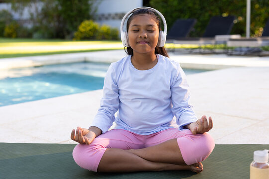 African American child sitting on mat by pool wearing pink leggings, white headset and water bottle