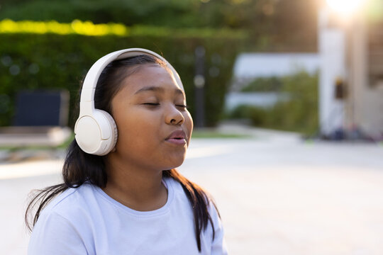 Youth African American female singing and mouthing words on patio wearing white tee and headphones