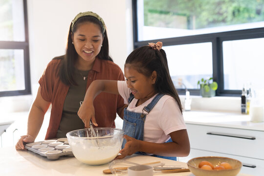 Asian mother and African American youth daughter mixing batter at counter with glass bowl and whisk