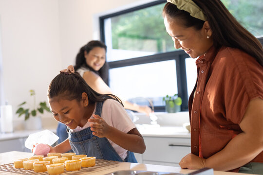 African American family watching teenage girl decorating cupcakes on kitchen island with piping bag