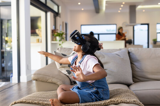 Diverse female family watching child wearing VR headset reaching forward on sofa in living room