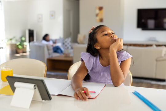 African American mother and daughter at home, child studying at white table with tablet