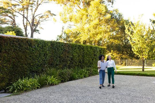 Diverse women coworkers walking, discussing plans in gravel courtyard wearing workwear, copy space