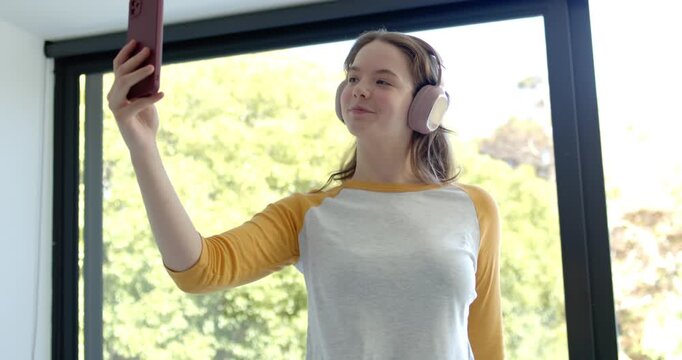 Woman in raglan-shirt tapping purple phone with pink-headset raising it onehanded by window singing