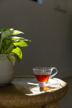 Clear glass teacup sitting on round wooden side table near window, casting warm reflections