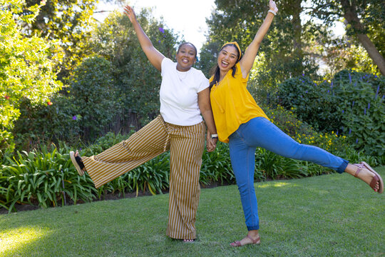 African American female friends holding hands posing in backyard on manicured lawn wearing sandals
