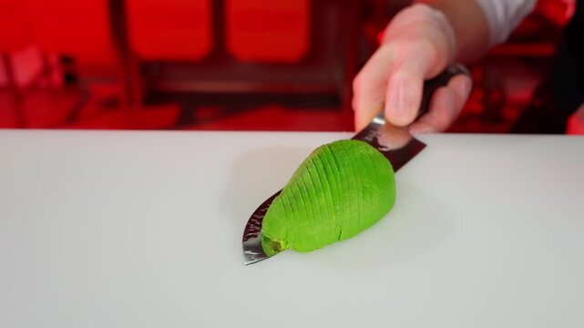 Chef cuts fresh green avocado with sharp knife. Cooking concept.