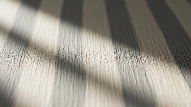 Sunlight streams across a textured ribbed surface featuring alternating bands of pale neutral and dark charcoal gray, creating a visually striking interplay of light and shadow that suggests