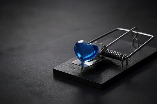 Blue heart on a mousetrap against dark background symbolizing love danger and relationship risk
