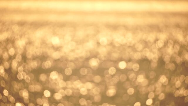 Golden shimmering water sparkling sunlight creating beautiful bokeh reflections on calm ocean surface abstract background for luxury or serenity