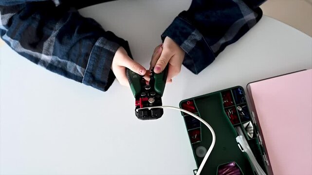 Student testing and crimping wire connections with professional tool at organized home workspace, quality check during electronics project showing practical STEM skills and hands on remote learning