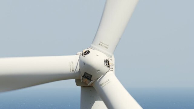 Wind turbine blades rotating in a close-up view against a clear blue sky over the ocean, generating clean and sustainable electrical power from the wind for a greener future