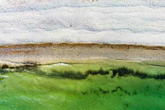 Top down aerial view of the southern end of Keel Beach on Achill Island, County Mayo, Ireland. White pebbles meet clear green Atlantic water in an abstract coastal pattern.