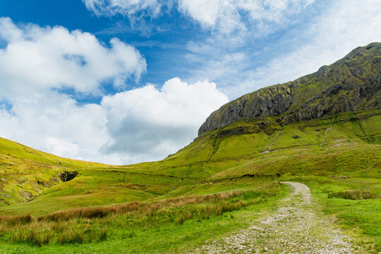 Gleniff Horseshoe in County Sligo, Ireland, with rolling grassland beneath steep limestone mountains and bright clouds. A scenic drive through one of Irelands classic valleys.