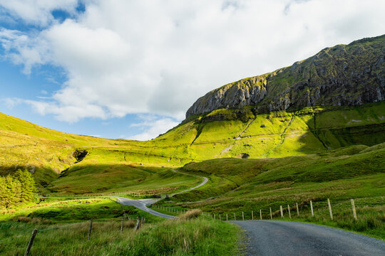 Gleniff Horseshoe in County Sligo, Ireland, with rolling grassland beneath steep limestone mountains and bright clouds. A scenic drive through one of Irelands classic valleys.
