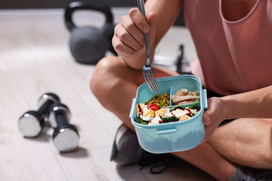 Athletic young man with tasty salad and eggs in lunch box indoors, closeup