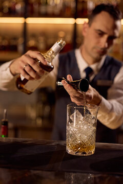 Close up of bartender pouring drink into cocktail glass filled with ice.