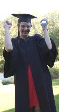 Vertical video: Female graduate after ceremony cheering, raising diploma and pumping on quad in cap