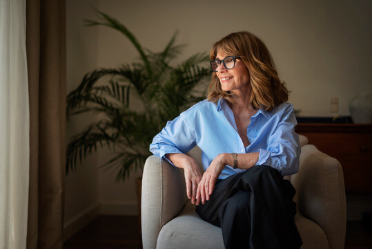 Portrait of a stylish mid aged woman sitting in an armchair in a minimalist home