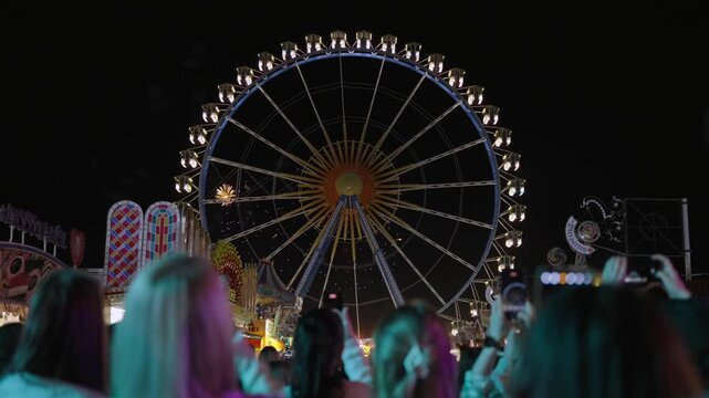 Munich, Germany. Spektakulaeres Feuerwerk steigt ueber der Theresienwiese in Muenchen, Deutschland, auf, waehrend Menschen die Show und die hellen Lichter des Volksfests erleben.