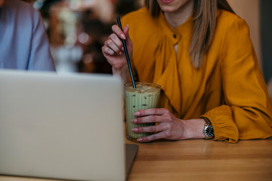 Woman drinking iced matcha latte working on laptop