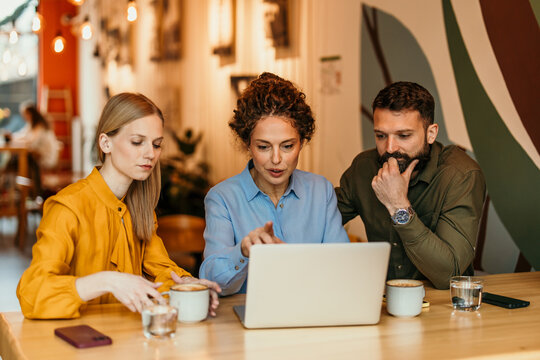 Coworkers collaborating on laptop discussing business at cafe