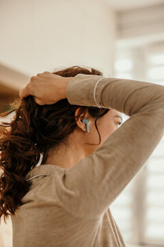 Woman styling hair wearing wireless earbud in morning