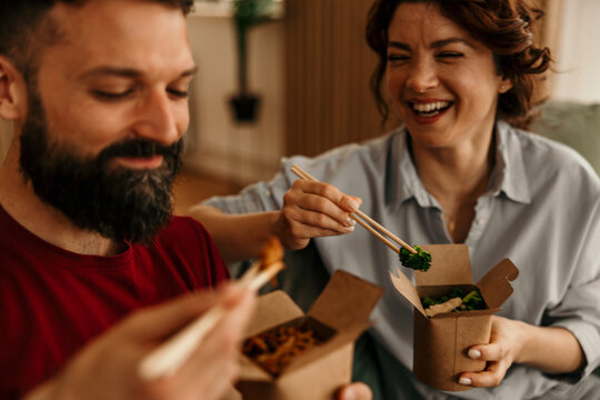 Couple laughing, enjoying takeout food at home