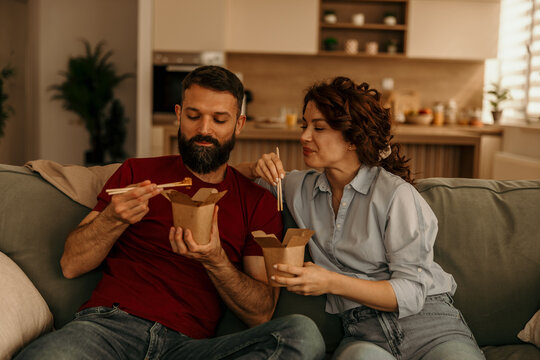Couple enjoying takeout food with chopsticks at home