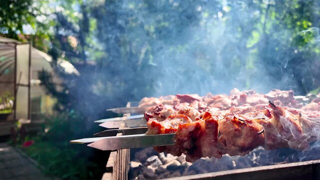 Slow motion closeup of juicy meat skewers grilling on hot charcoal with smoke and fire in sunny backyard barbecue setting