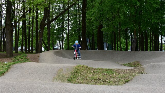 Young boy cycling on a pump track bicycle course in a green city park. Active outdoor childhood, healthy lifestyle, sport activities and fun recreation for children during springtime.
