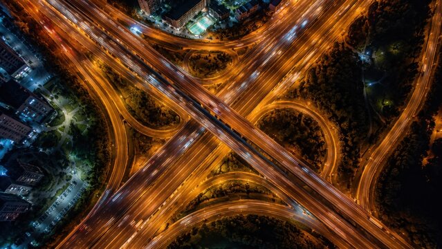 Aerial view of a complex highway interchange at night with glowing lights and moving vehicles