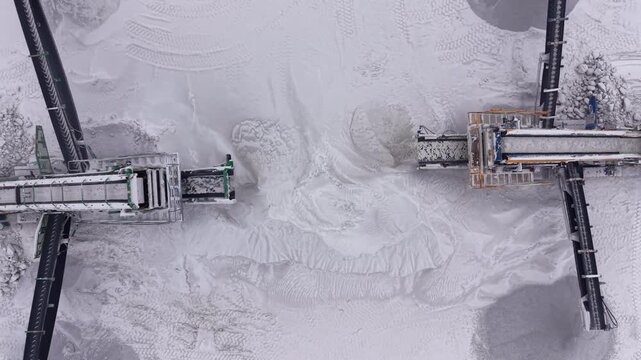 Top-down view of two mobile screener machines processing white gypsum mineral at an open-pit quarry, with conveyor belts and dust visible on the powdery surface